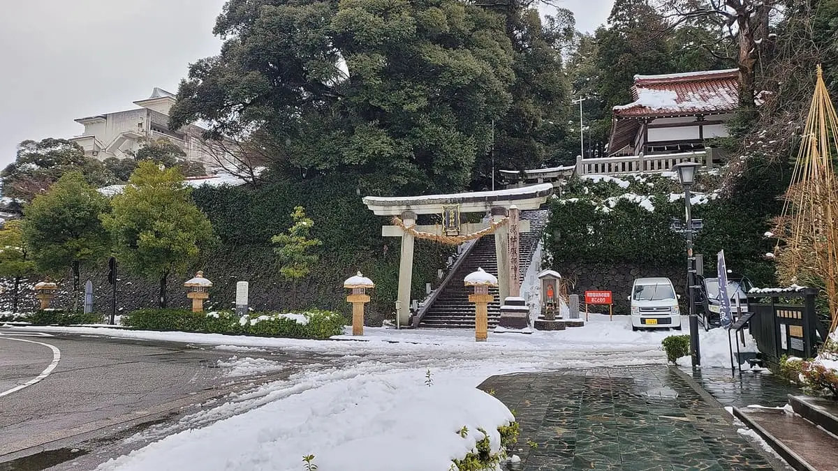 Snowy road leading to a shrine gate and temple steps in Yamashiro Onsen