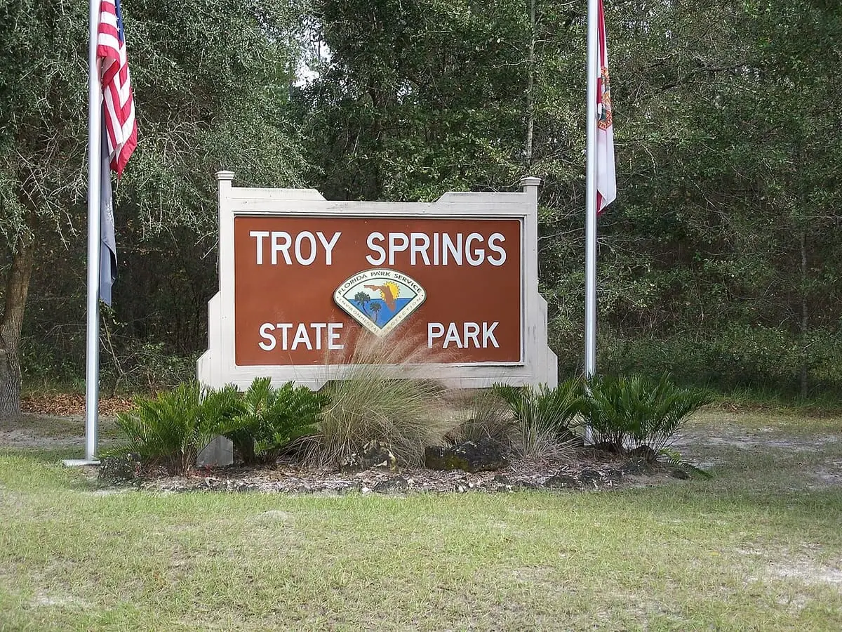Troy Springs State Park entrance sign between flagpoles in front of woods