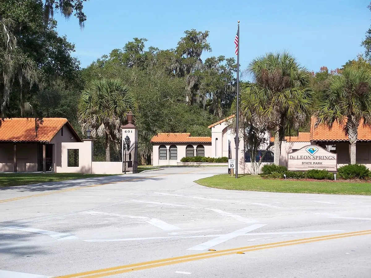 De Leon Springs State Park entrance with Spanish style buildings, palms and a flagpole