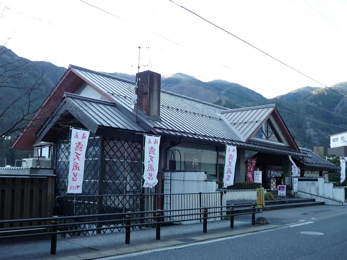 Wooden building of the Gero Onsen Kur Garden open air bath under wooded hills