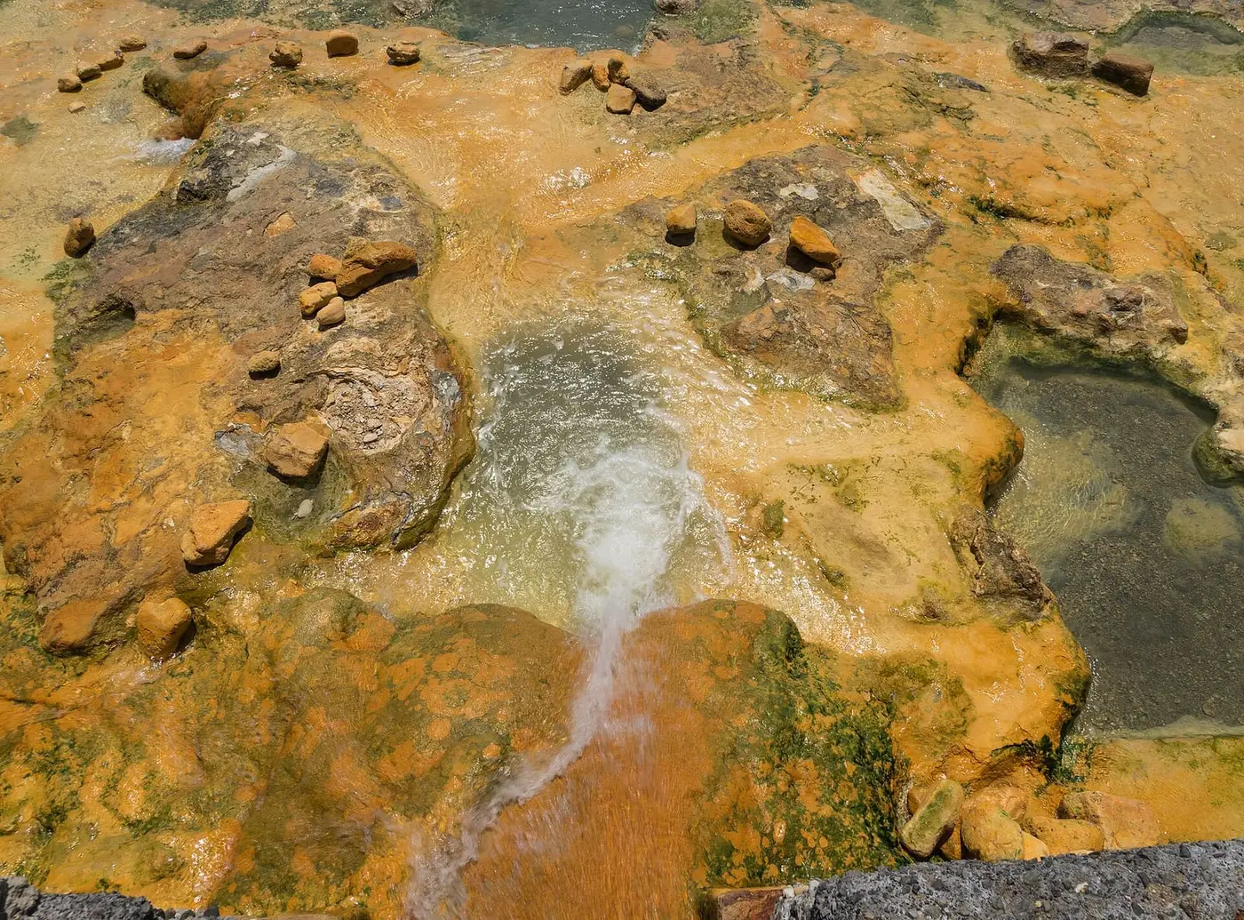 Hot spring water flowing over orange mineral crusted rock at Loutra Edipsou on Evia