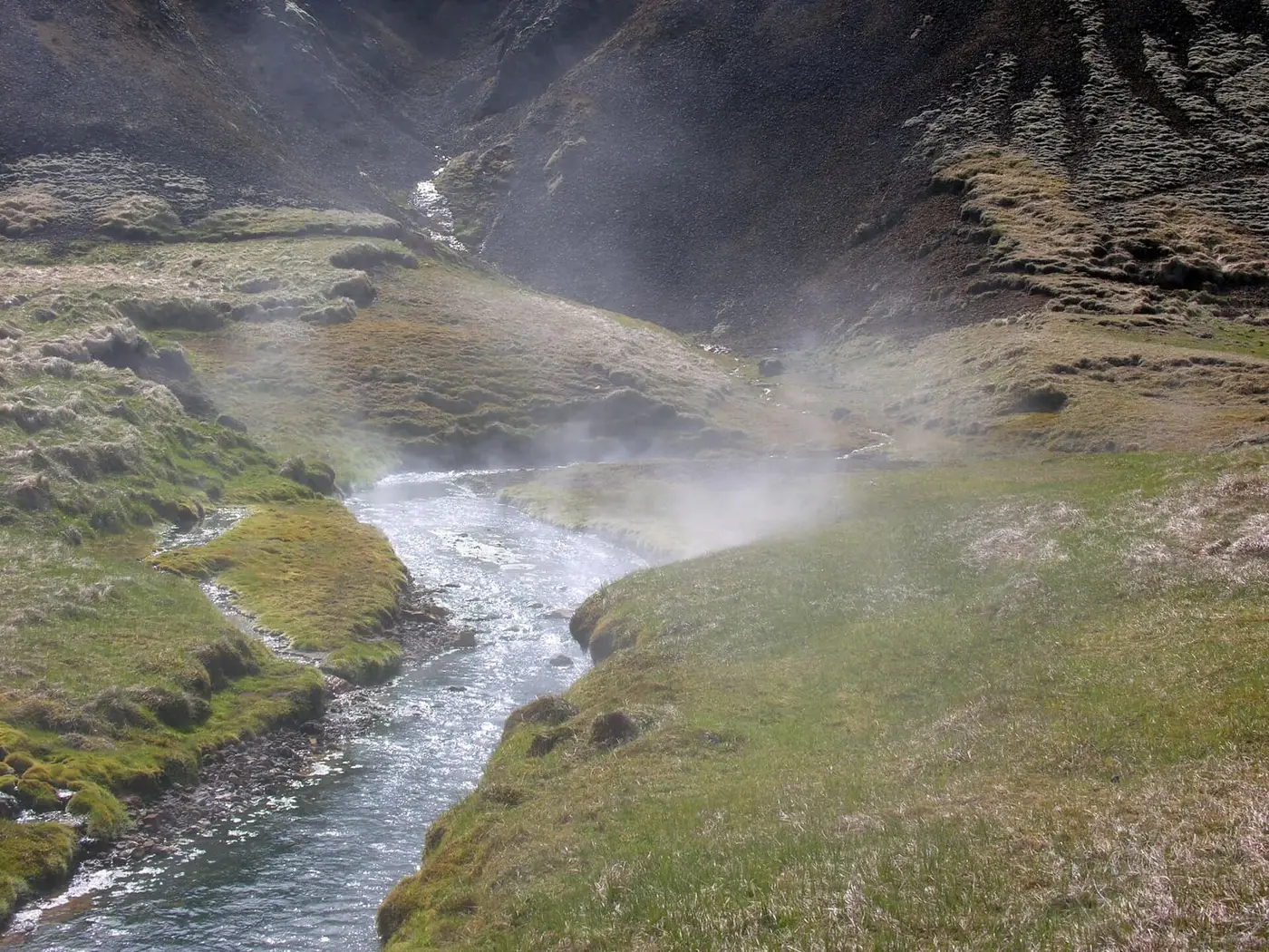 Steam rising from the warm Reykjadalur river as it winds through a green valley