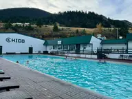 Large outdoor hot pool at Chico Hot Springs below white buildings with the Chico name and forested hills