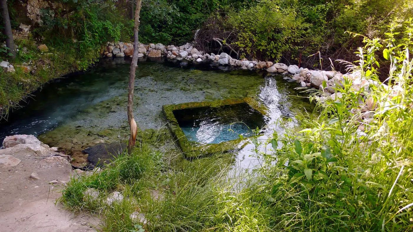 Clear hot spring pool edged with stones and green plants at Loutra Eleftheron near Kavala