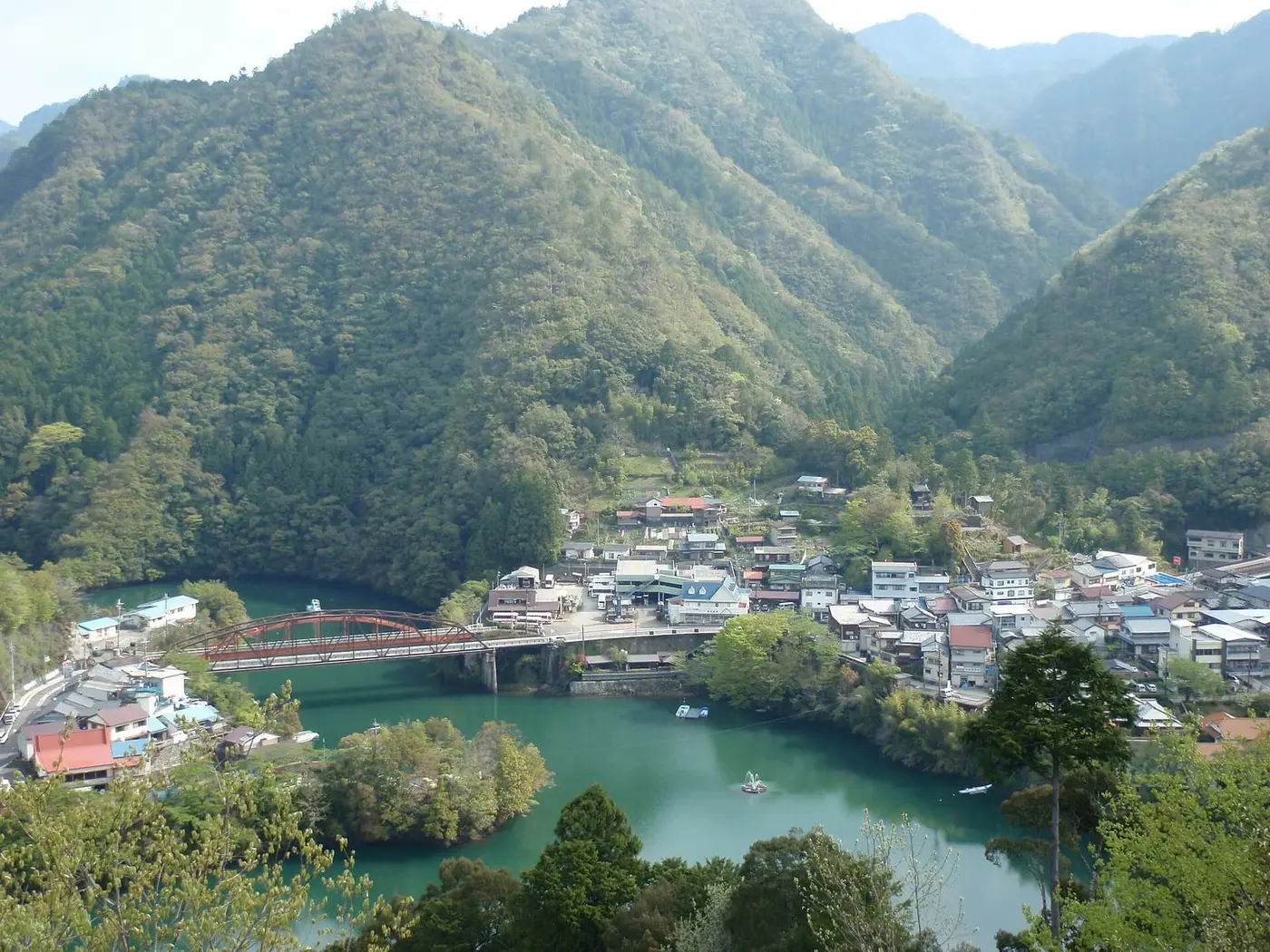 Totsukawa Onsen town beside the green waters of Lake Futsuno, surrounded by forested mountains