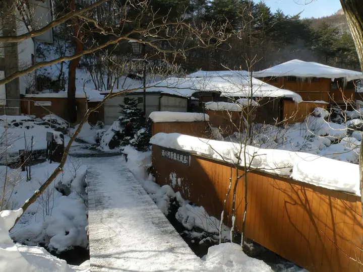Snowy wooden walkway leading to the Sainokawara Rotenburo bath buildings in Kusatsu