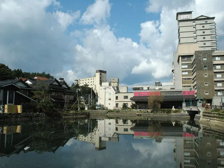 Hotels of Wakura Onsen reflected in still water under a cloudy blue sky