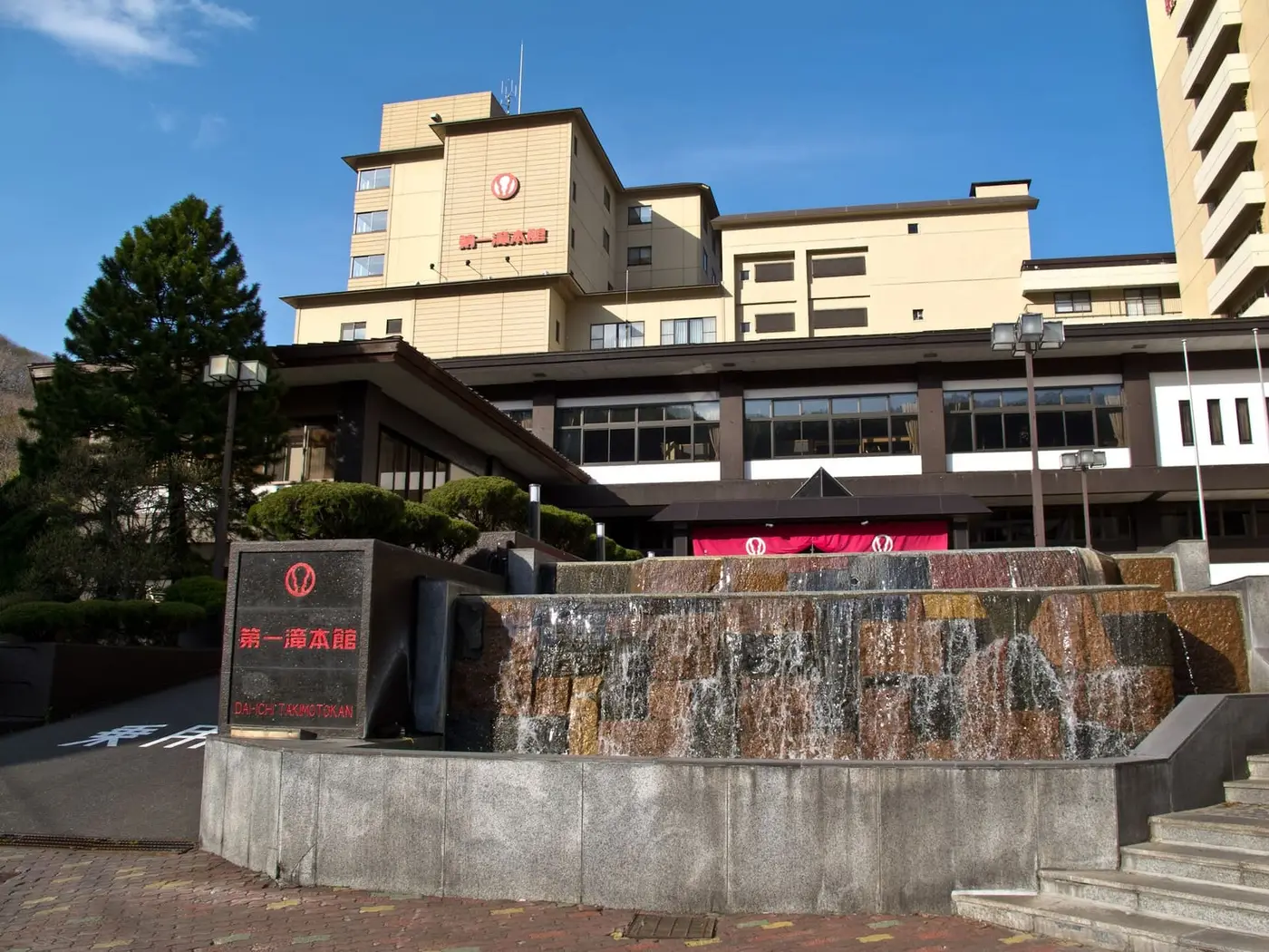 Entrance of Dai-ichi Takimotokan hotel in Noboribetsu with a stone fountain and tall hotel wings