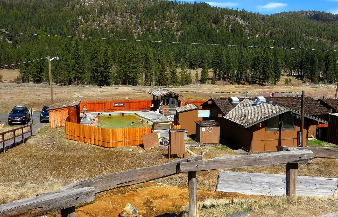 Fenced hot spring pool complex at Grover Hot Springs State Park below pine covered hills