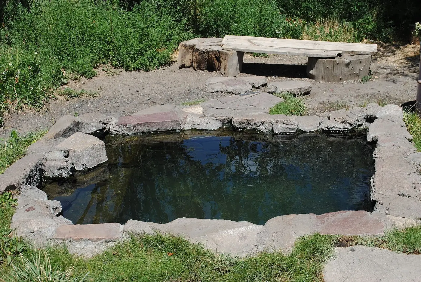 Stone lined soaking pool known as The Cube at Montezuma Hot Springs with a wooden bench behind
