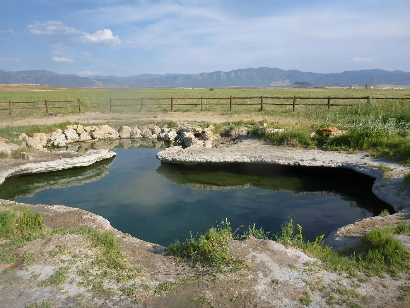 Clear travertine pool at Meadow Hot Springs in a fenced farm field below desert mountains