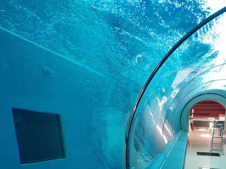 Glass walkway tunnel running through the blue water of the deep diving pool at Terme Millepini
