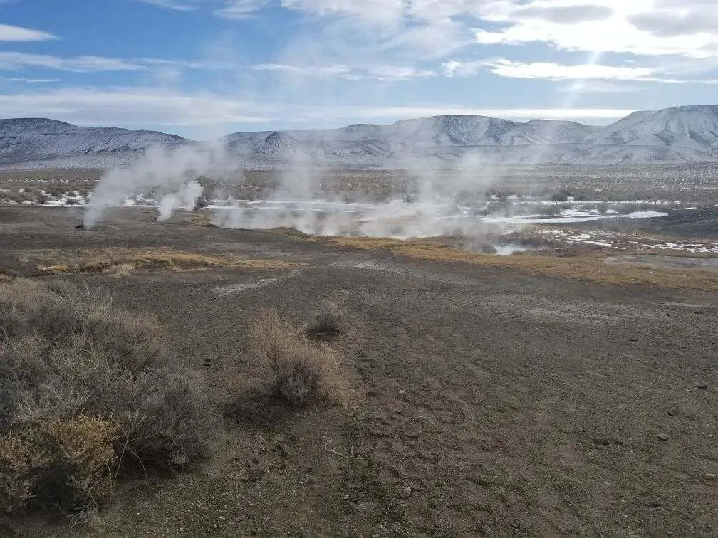 Steam rising from the geothermal field at Mickey Hot Springs with desert mountains behind
