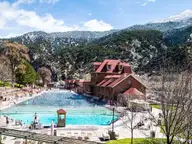 Glenwood Hot Springs Pool with its red roofed bathhouse below snow dusted mountains on a sunny day