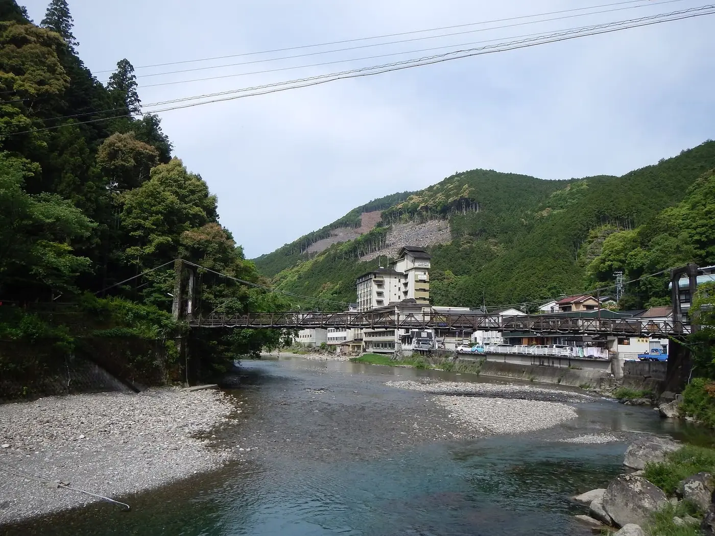 Oto River gravel banks at Kawayu Onsen with the village and a footbridge below wooded hills