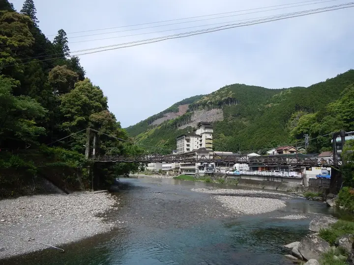 Oto River gravel banks at Kawayu Onsen with the village and a footbridge below wooded hills