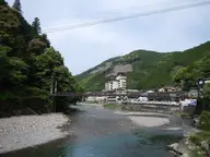 Oto River gravel banks at Kawayu Onsen with the village and a footbridge below wooded hills