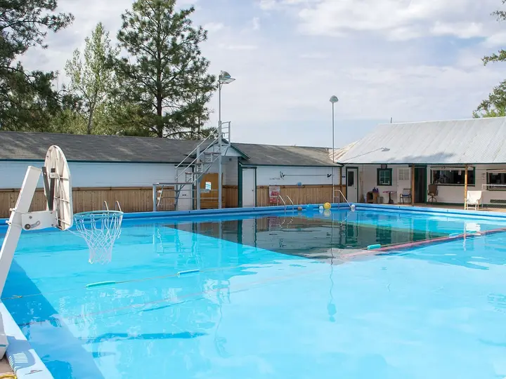 Cove Warm Springs Pool, a large clear blue outdoor pool beside low white buildings