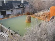 Green mineral pool at Mystic Hot Springs beside orange travertine mounds and frosted brush
