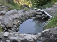 Rock rimmed soaking pool fed by white piping at Skinny Dipper Hot Springs