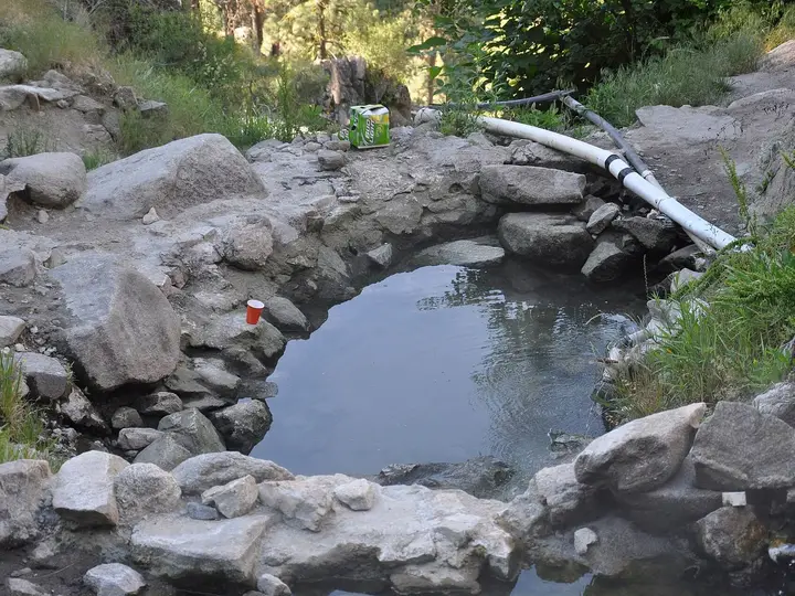 Rock rimmed soaking pool fed by white piping at Skinny Dipper Hot Springs