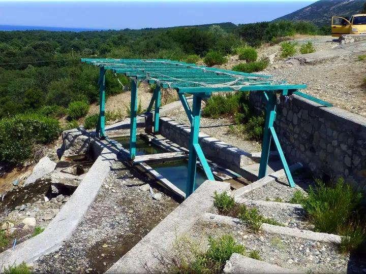 Small open air thermal pool under a green pergola among hillside shrubs at Therma, Samothraki