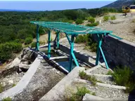 Small open air thermal pool under a green pergola among hillside shrubs at Therma, Samothraki