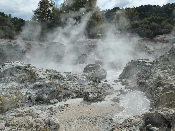 Steam rising over grey rocks and hot pools across Hell's Gate toward the Inferno Pools