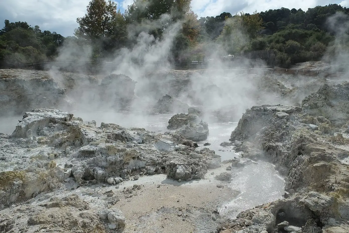 Steam rising over grey rocks and hot pools across Hell's Gate toward the Inferno Pools