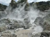 Steam rising over grey rocks and hot pools across Hell's Gate toward the Inferno Pools