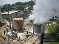 Steam billowing from hot spring wellheads and pipes among buildings at Kirishima Onsen