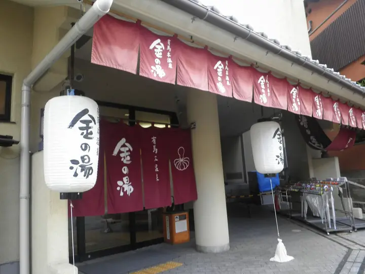 Entrance of Kin no Yu bathhouse in Arima Onsen with red noren curtains and white paper lanterns