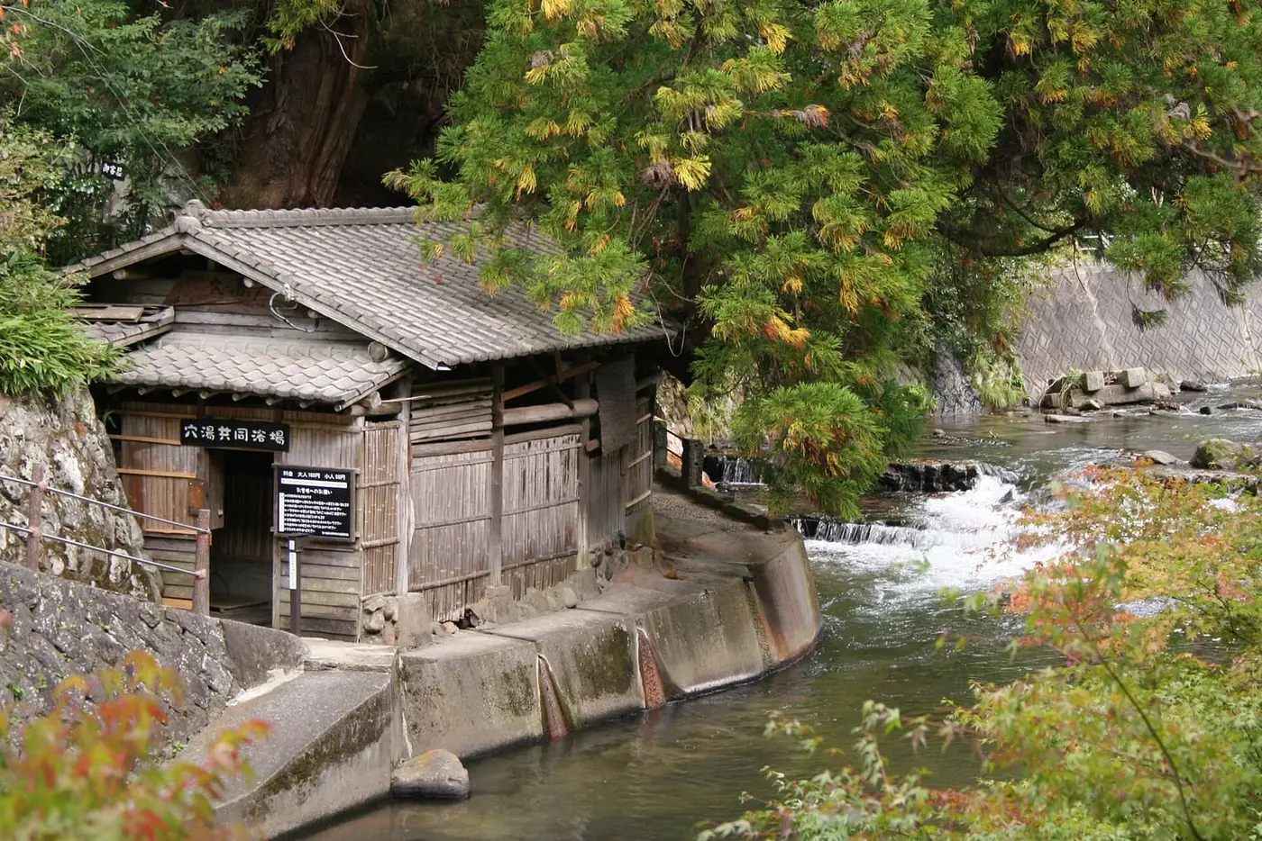 Wooden riverside bathhouse beside the rushing Tanohara River at Kurokawa Onsen in autumn