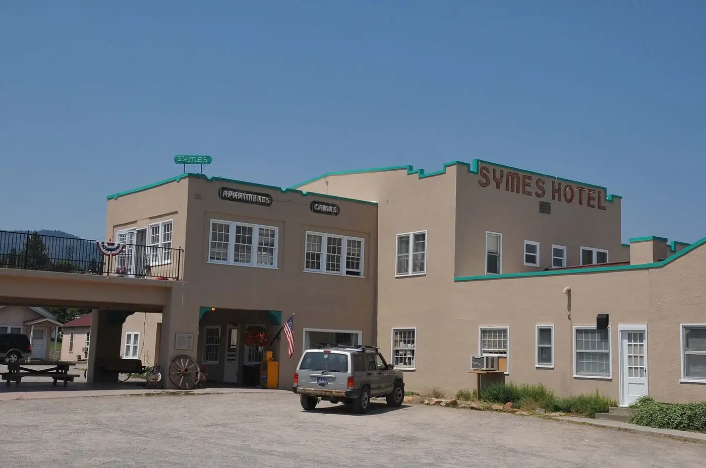 Tan Mission style Symes Hotel with green trim and its name on the roofline in Hot Springs, Montana