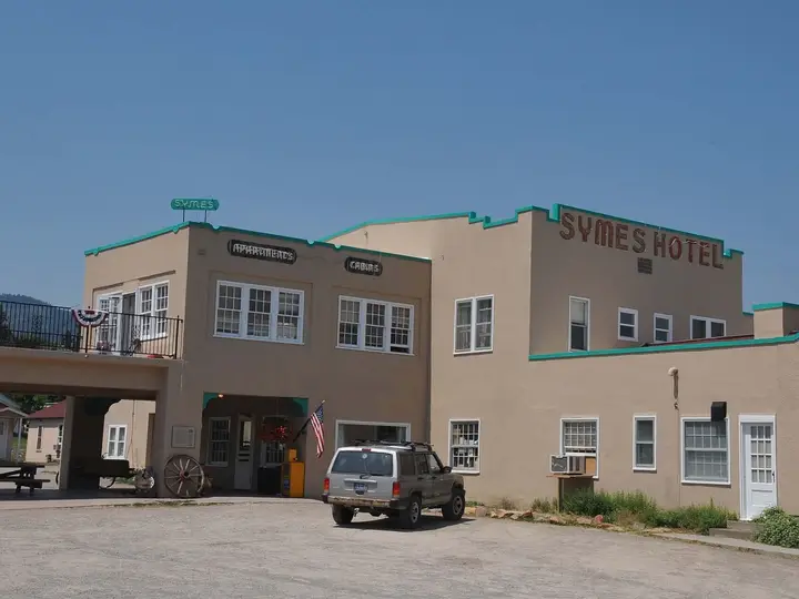 Tan Mission style Symes Hotel with green trim and its name on the roofline in Hot Springs, Montana