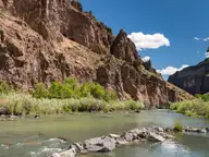 Owyhee River flowing over rocks below tall red canyon cliffs at Snively Hot Springs