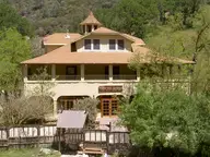 Front of the historic Wilbur Hot Springs lodge with wraparound porch below wooded hills