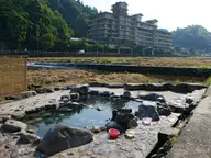 Rock lined Kawara buro open air bath beside the Mitoku River with a large hotel behind at Misasa Onsen
