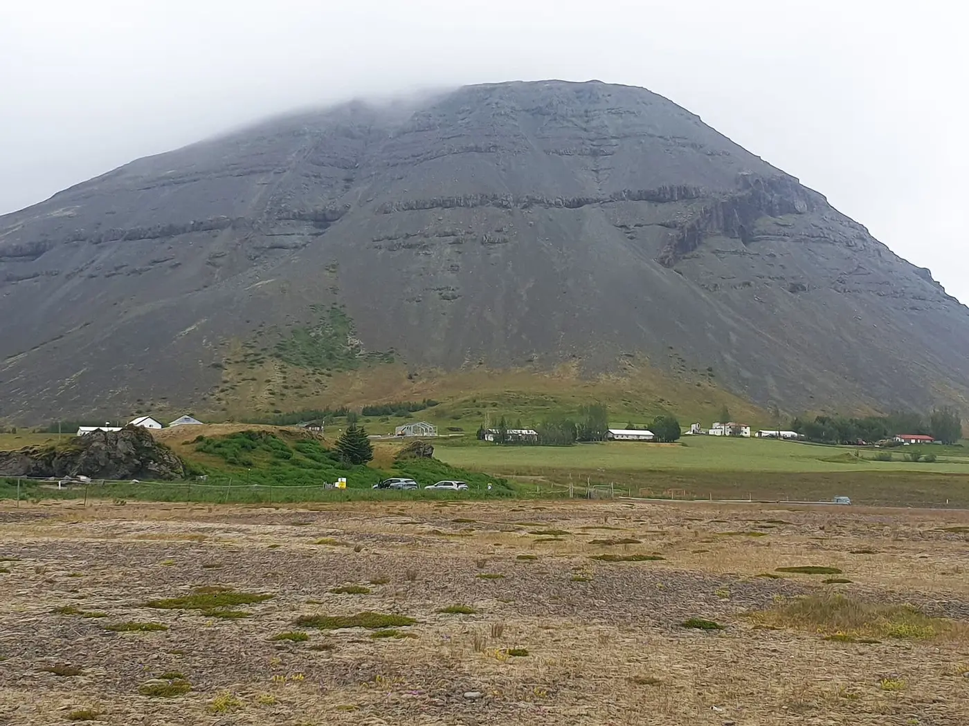 Grey mountain rising above the farmland at Hoffell in southeast Iceland under low cloud