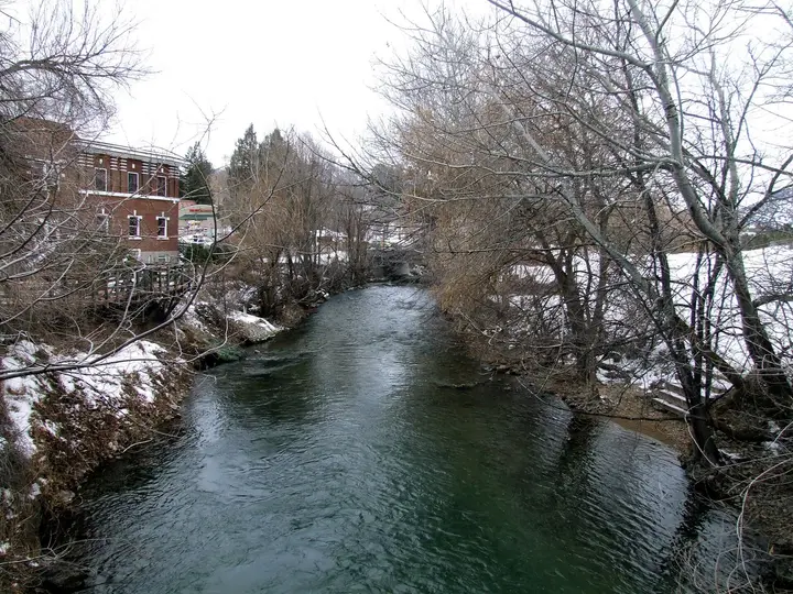 Portneuf River flowing past a brick building and bare winter trees in Lava Hot Springs