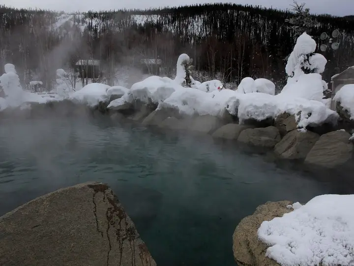 Steaming rock lined hot springs lake under heavy snow at Chena Hot Springs Resort