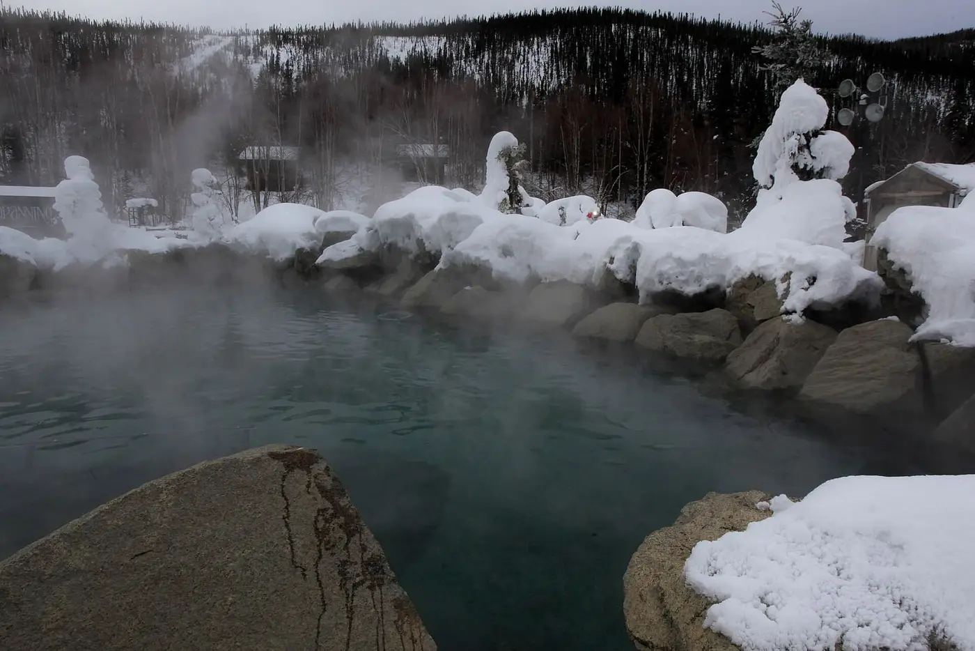Steaming rock lined hot springs lake under heavy snow at Chena Hot Springs Resort