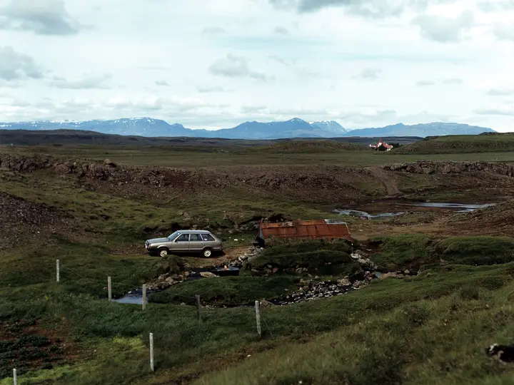 Small rusty roofed hut and warm stream at Hrunalaug with the Hruni farm and mountains beyond