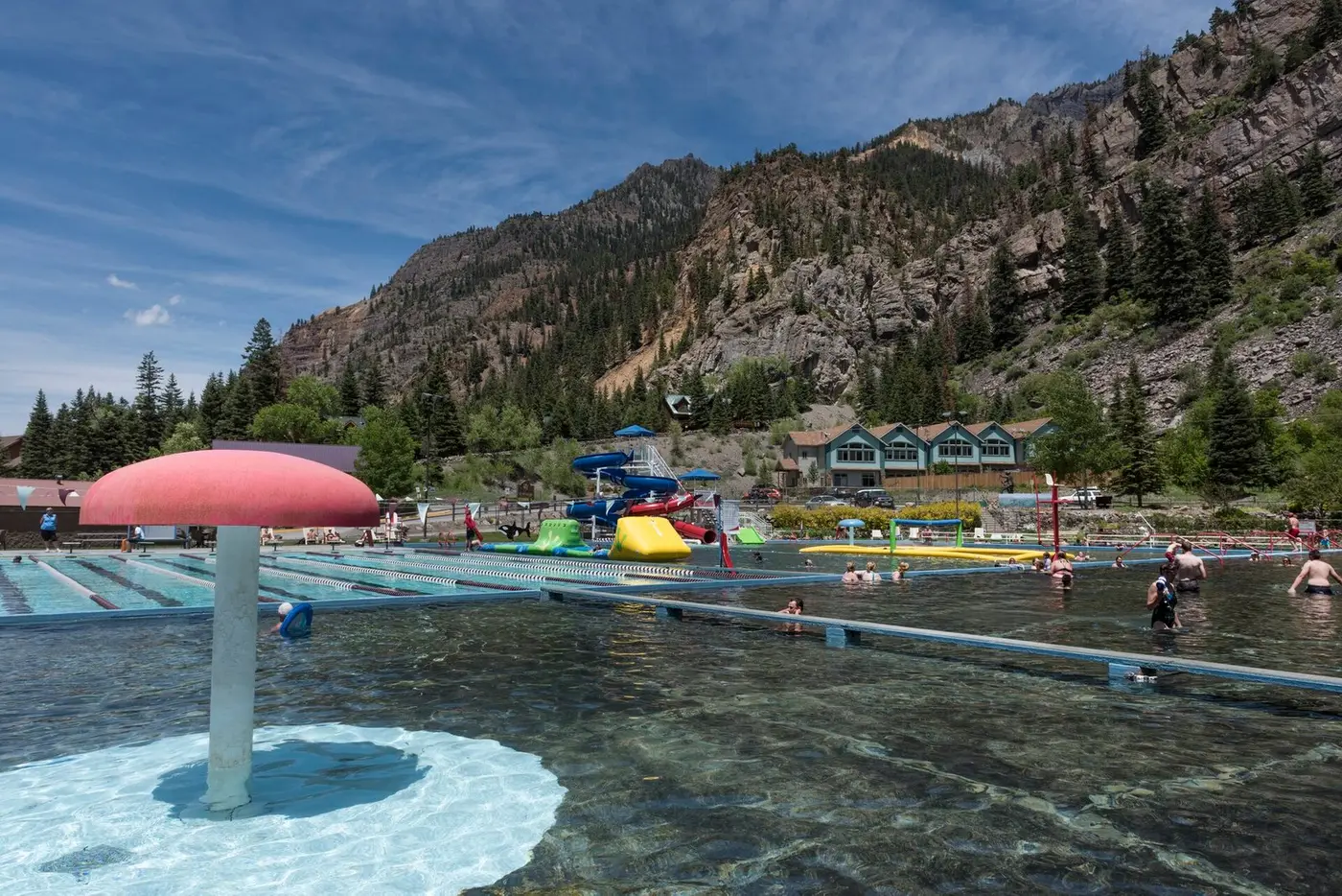 Large outdoor hot springs pool with a mushroom fountain below the red cliffs of Ouray