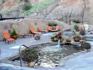 Mineral pool with clay pot fountain and orange lounge chairs below sandstone cliffs at Ojo Caliente
