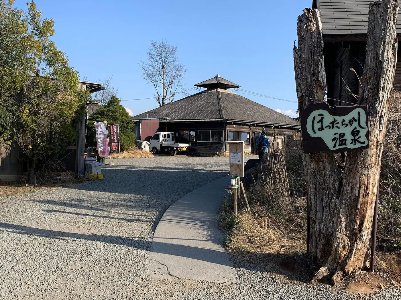 Gravel path and carved wooden sign at the entrance of Hottarakashi Onsen on a sunny day