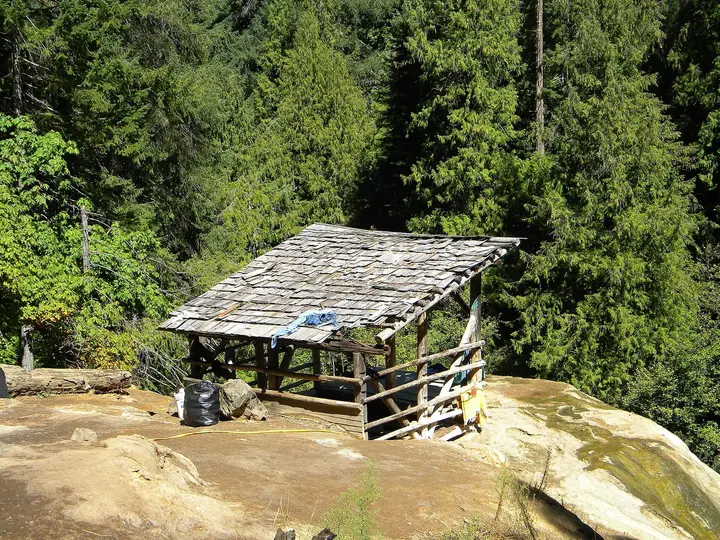 Weathered wooden shelter over the Umpqua Hot Springs soaking pool on a travertine ledge in conifer forest