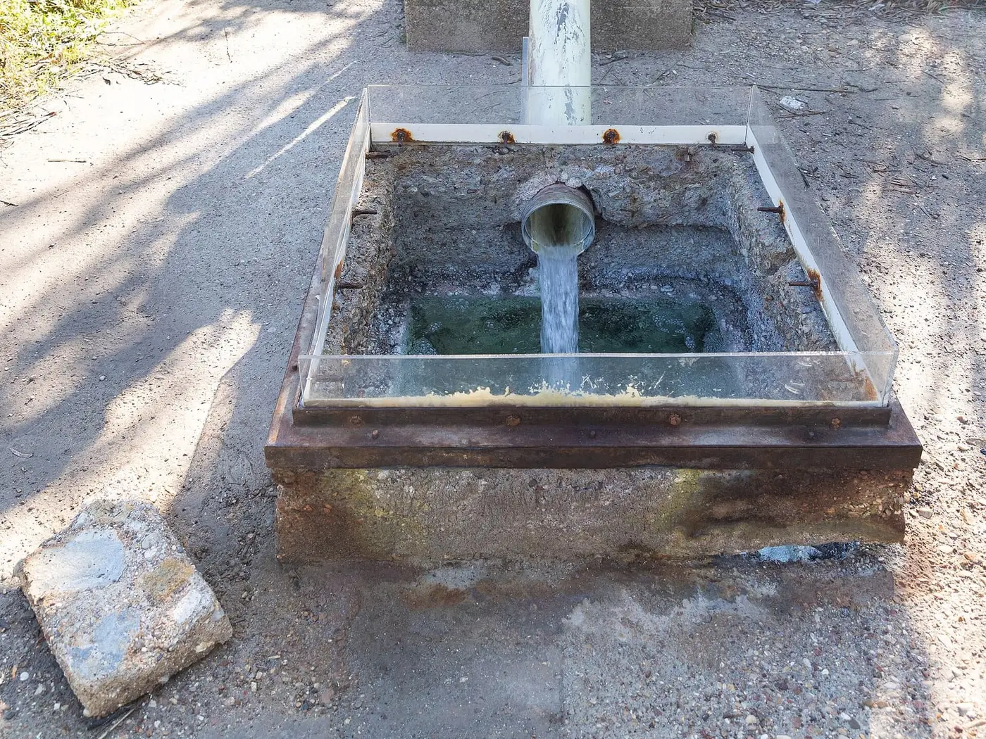 Sulphur spring water running from a pipe into a small concrete basin at Kyllini