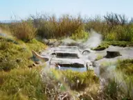 Steaming concrete soaking channels at Baker Hot Springs surrounded by grass and desert brush under blue sky