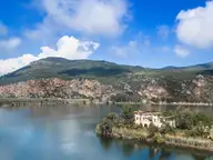 Lake Kaiafas with a wooded islet and old building below the cliffs of Mount Lapithas